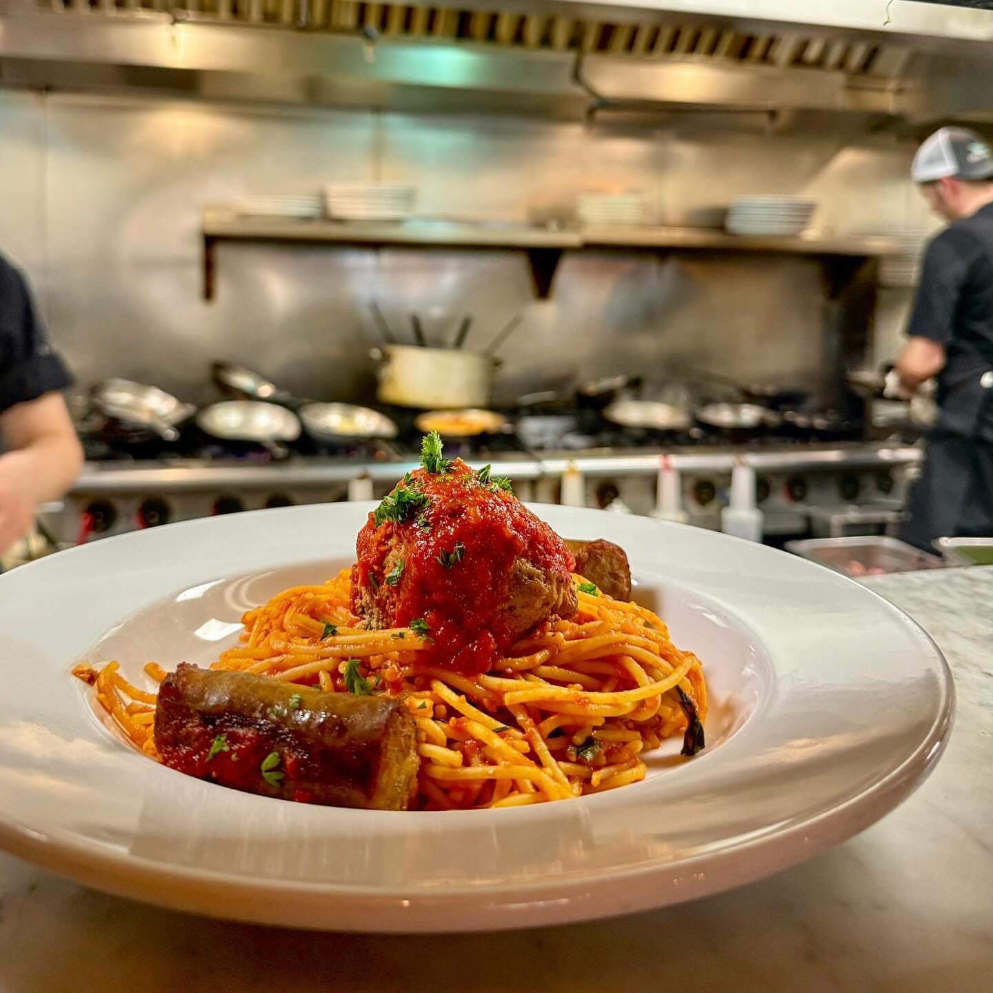 A plate of spaghetti on the pass with the kitchen line behind